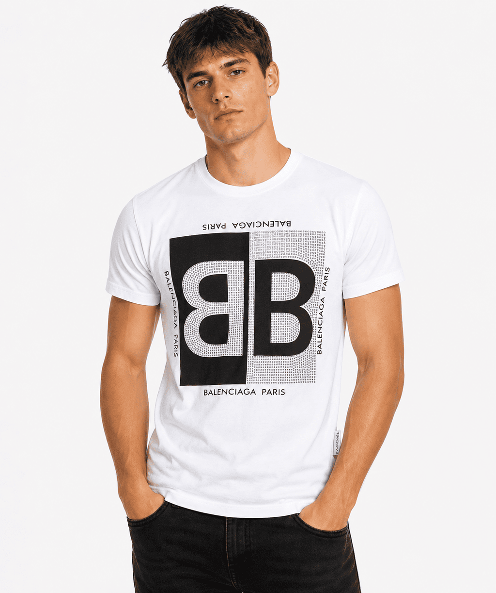 A man wearing a white Balenciaga Paris graphic t-shirt with a large black and white 'BB' logo on the front, paired with black jeans, against a light gray studio background.