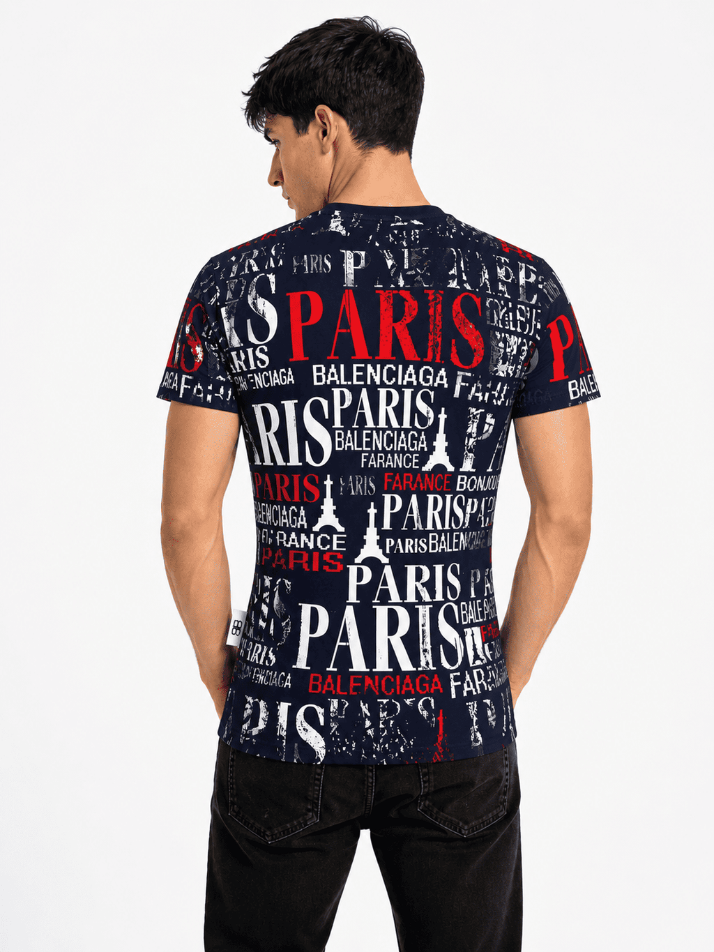 A man wearing a Balenciaga Paris t-shirt, viewed from the back. The shirt features a dark navy blue background covered in a collage print of 'PARIS' and 'BALENCIAGA' text in white and red, with the Eiffel Tower motif.