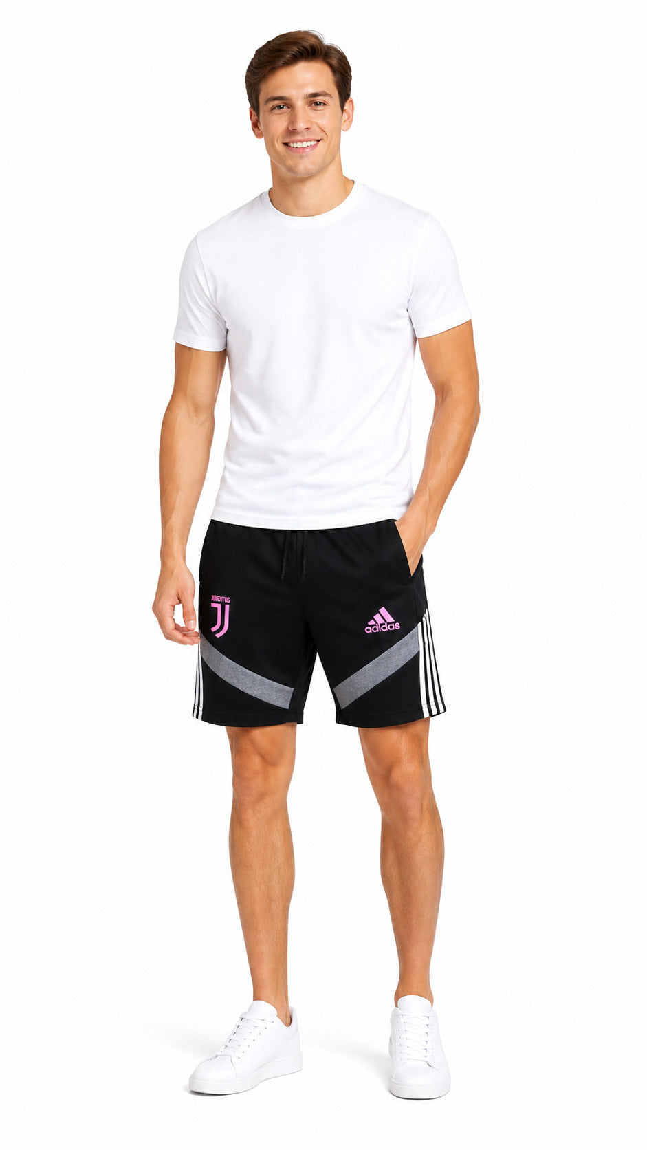 A man modeling black Adidas track shorts with white stripes and a pink Juventus logo, paired with a white t-shirt and white sneakers, on a white studio background.